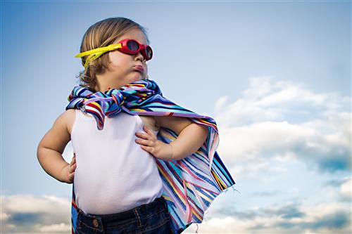 A child in a superhero pose with a cape