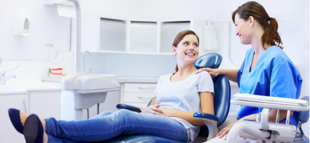 An orthodontist in a blue uniform warmly interacting with a young female patient reclining in a dental chair in a modern clinic setting.