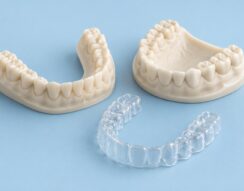 Illustration of two ivory dental arch models and a clear-aligner tray on a pale blue surface